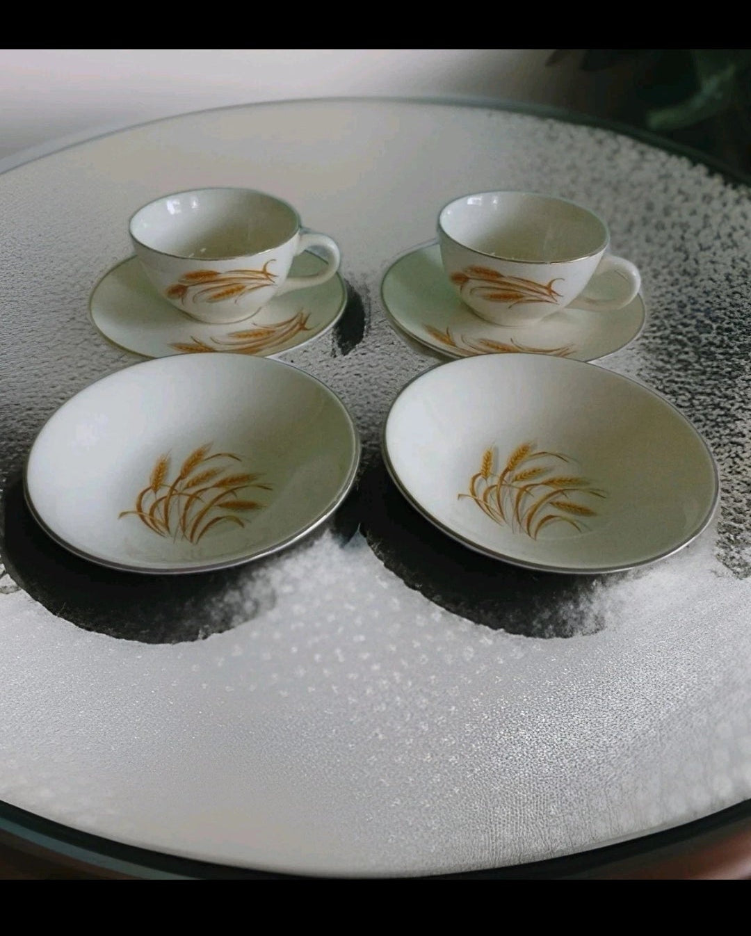 Set of white ceramic tea cups and saucers with gold patterns on a textured surface.