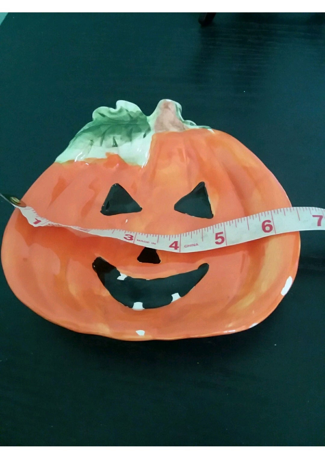 Paper plate shaped like a pumpkin with a face, featuring a tape measure on a dark background