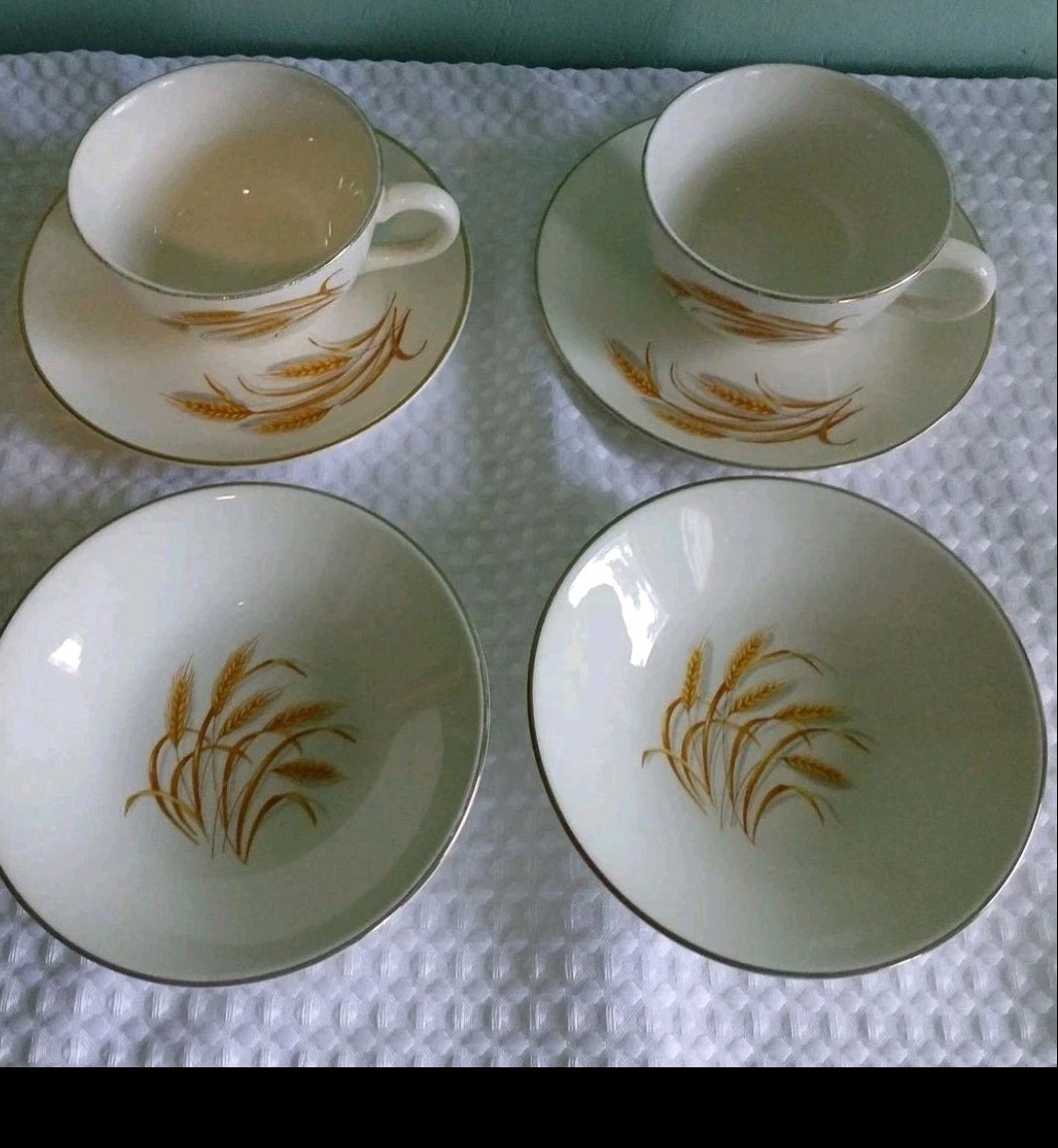 Set of ceramic tea cups and saucers with gold leaf design on a textured white surface.