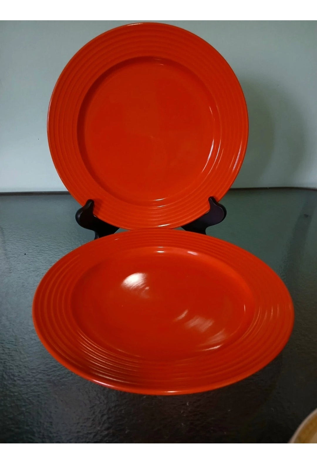 Two orange ceramic plates on a stand against a gray background