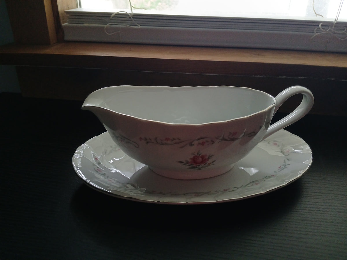 Pink floral gravy boat and saucer on a dark surface with a window in the background
