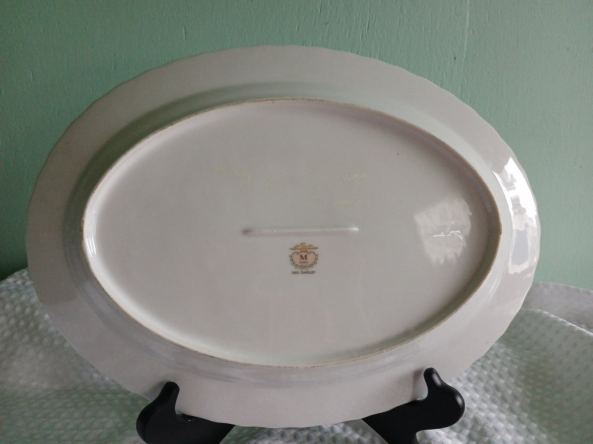 Oval ceramic plate with a logo on a stand against a green background