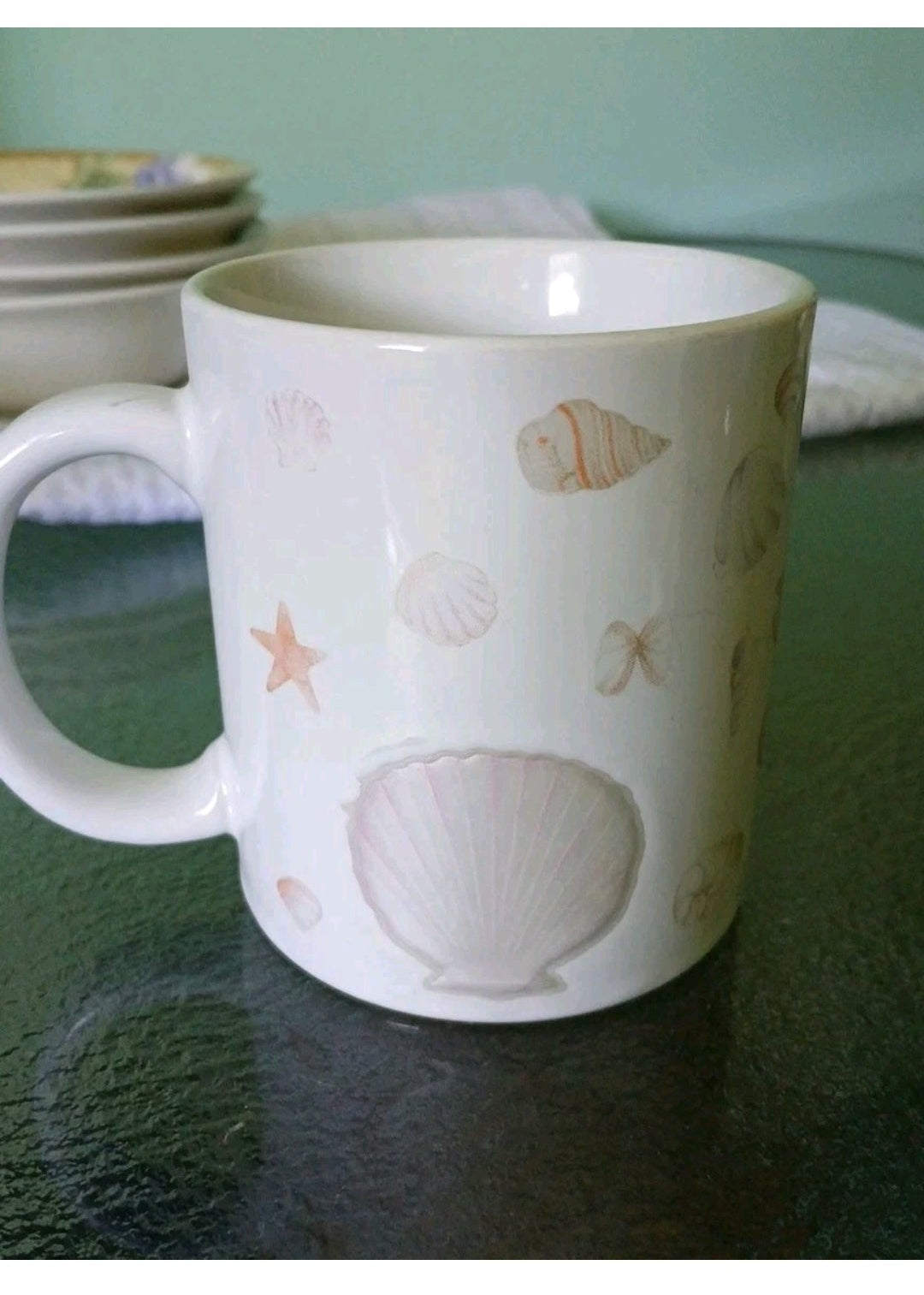 White mug with shell design on a green surface