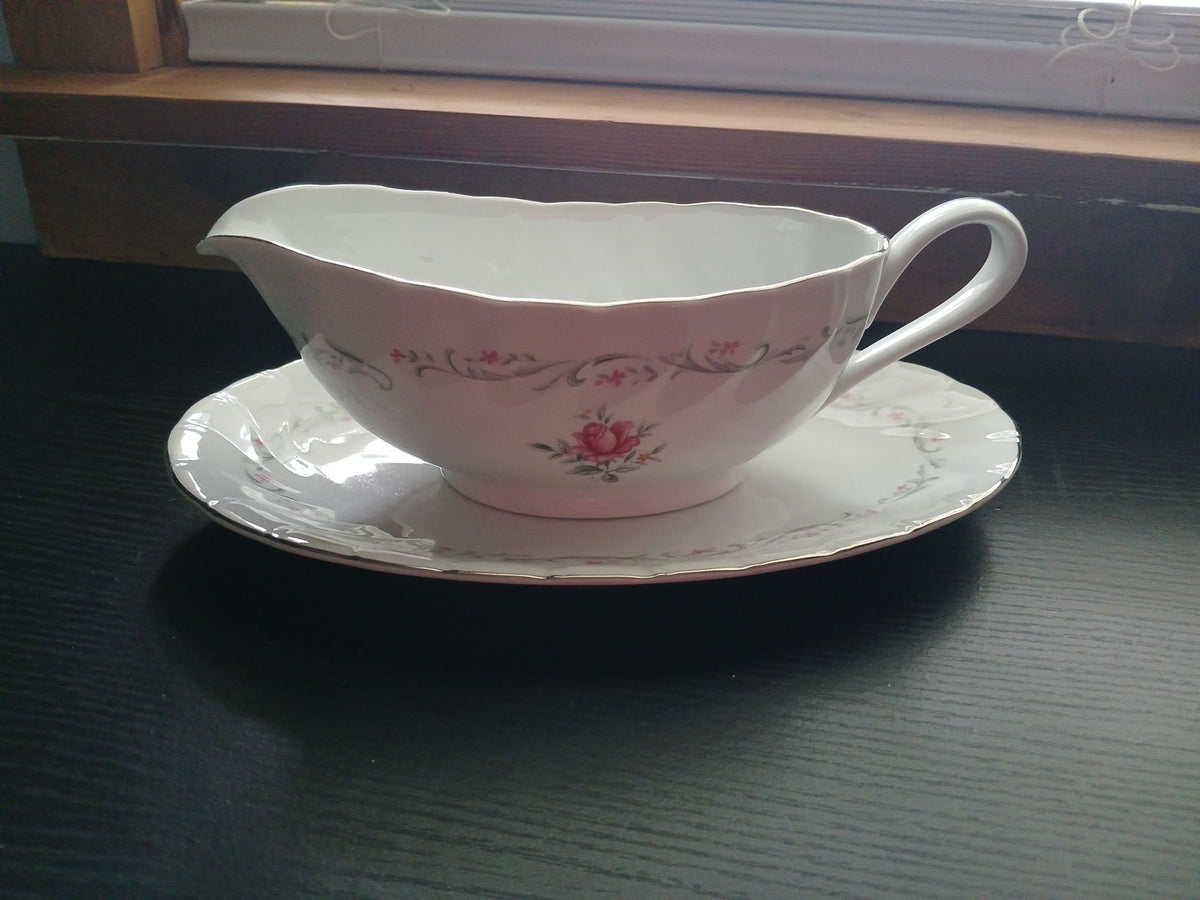White ceramic gravy boat with floral design on a matching saucer, placed on a dark surface.