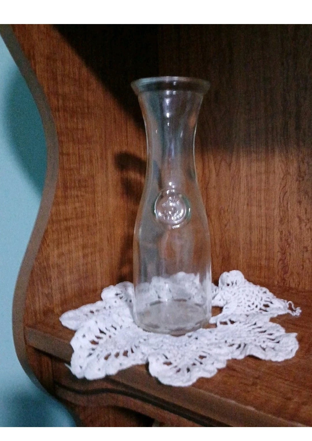 Clear glass vase on a white doily with a wooden surface background