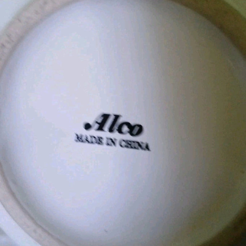 Close-up of a white ceramic item with 'Alco Made in China' text on a  white blurry blubackground