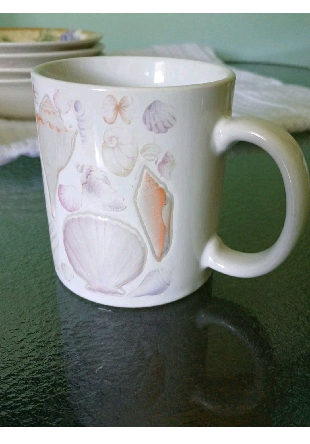 White mug with shell designs on a green surface