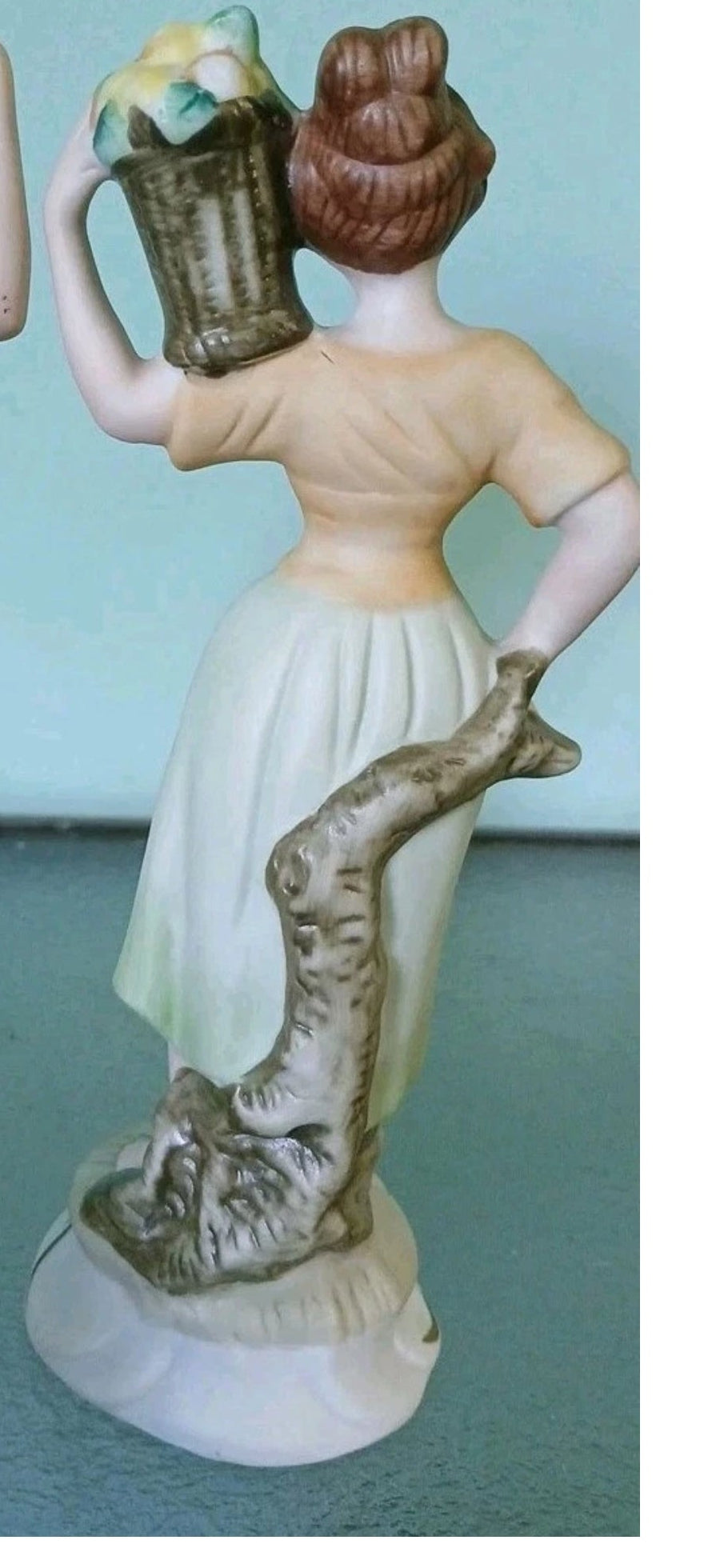 Decorative figurine of a woman with a basket on her head, standing against a log