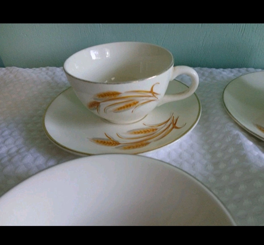 White teacup and saucer with gold patterns on a white tablecloth.