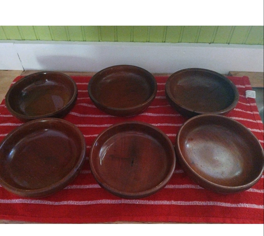 Set of six brown wooden bowls on a red and white striped towel with a green tiled wall background.
