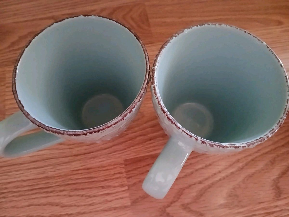 Two ceramic mugs with red rims on a wooden surface