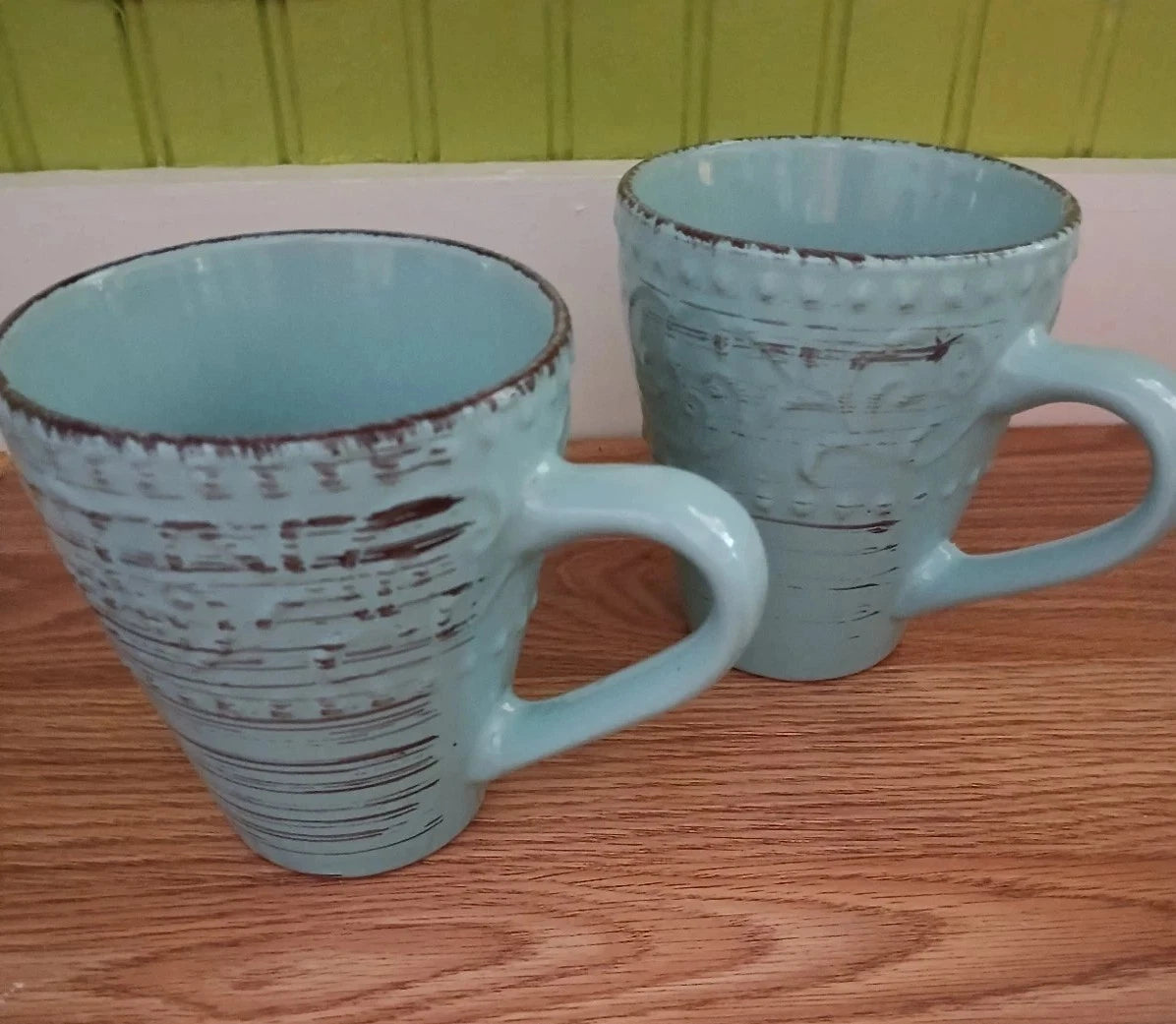 Two light blue mugs with textured design on a wooden surface.