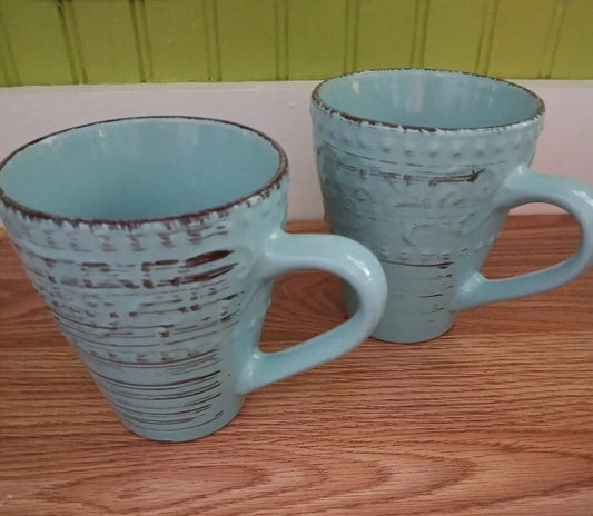 Two light blue mugs with textured design on a wooden surface.