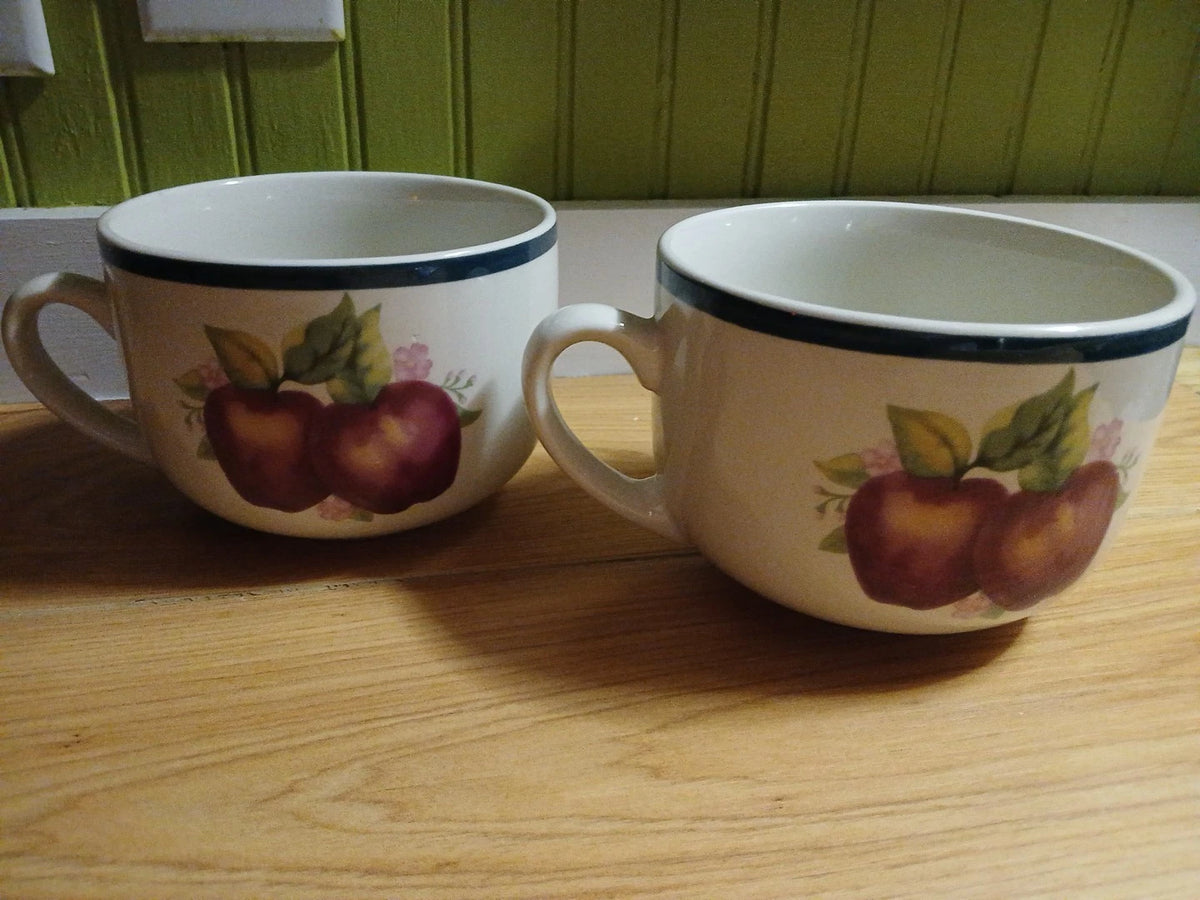 Two ceramic mugs with apple design on a wooden surface.