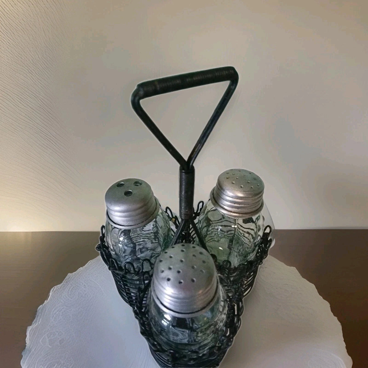 Set of three glass salt shakers with metal lids in a black wire holder on a white surface.