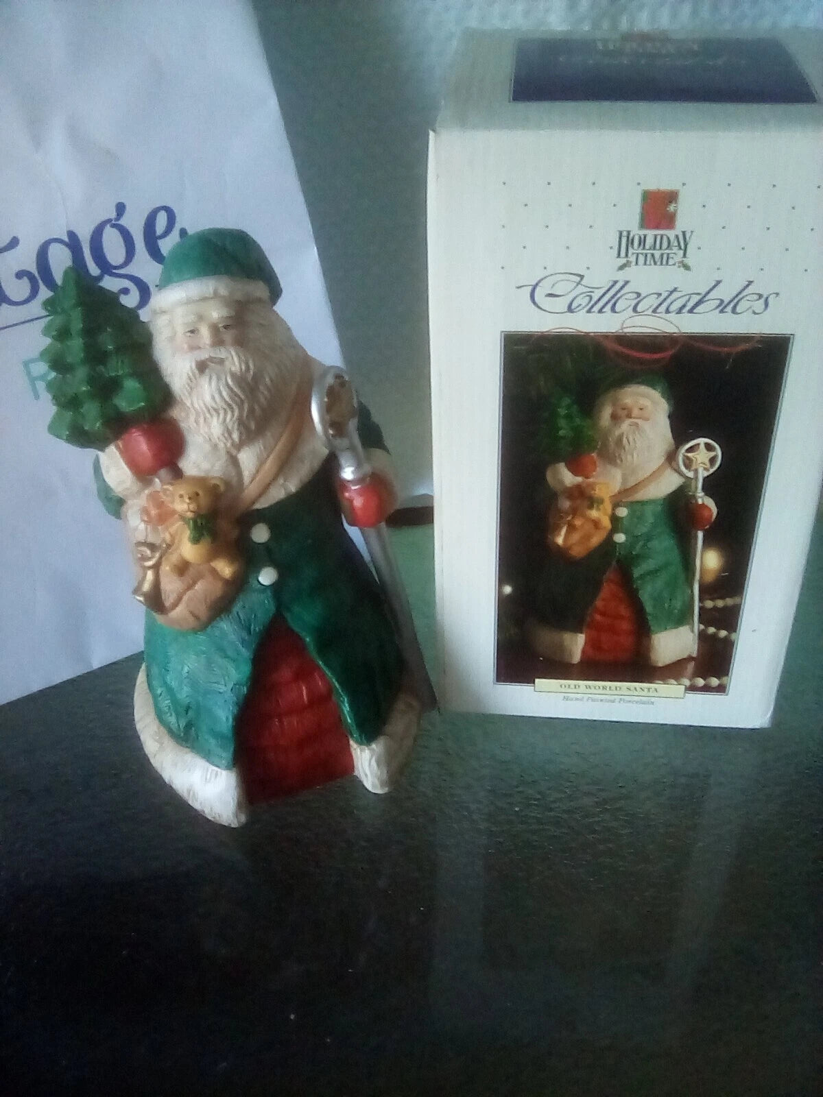 Christmas ornament of a Santa Claus figure with a box labeled 'Holiday Time Collectibles' on a dark surface.
