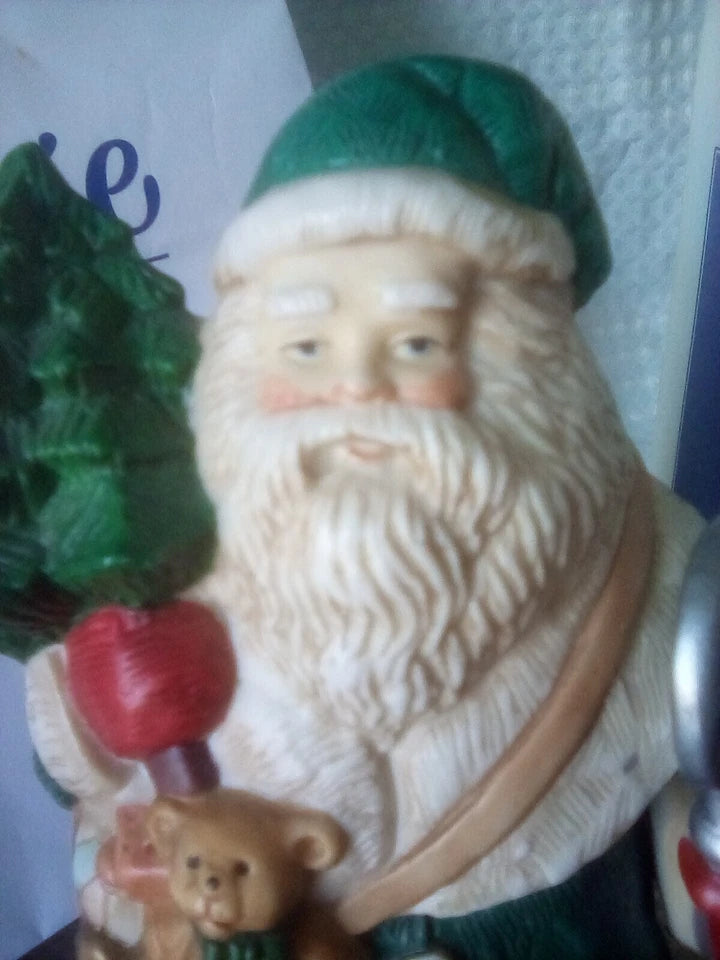 Decorative figure of a bearded man with a green hat, holding a teddy bear and a red apple, against a white background.