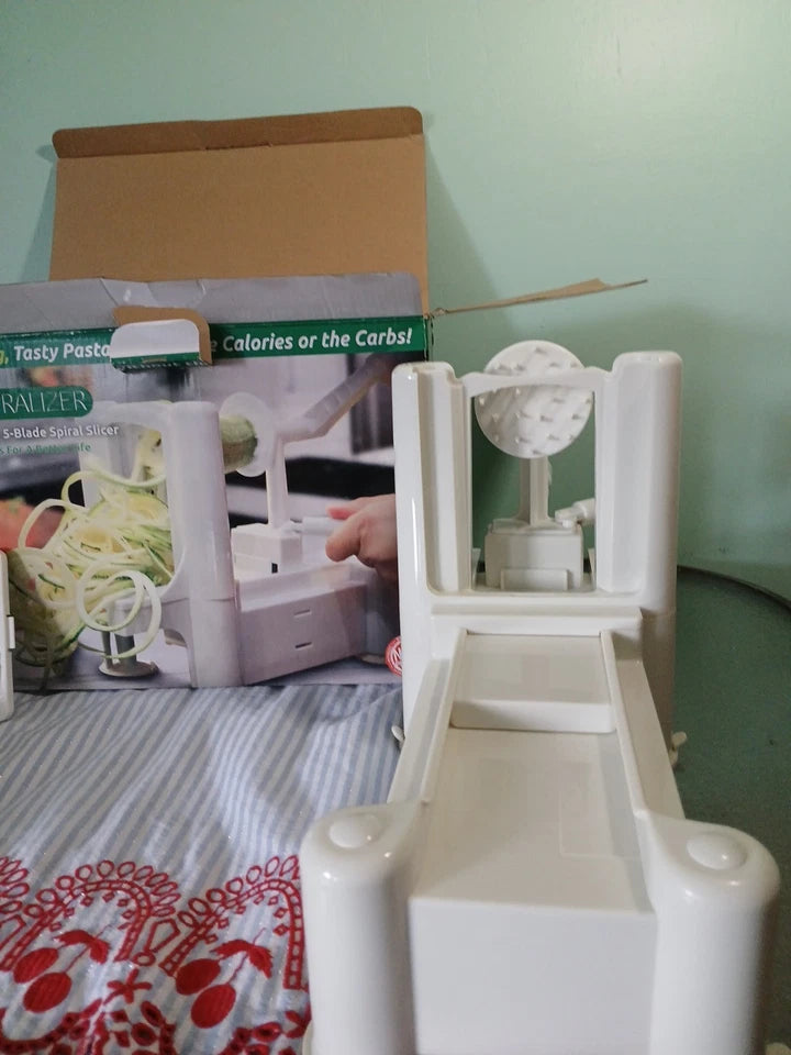 White spiralizer on a table with a cookbook in the background