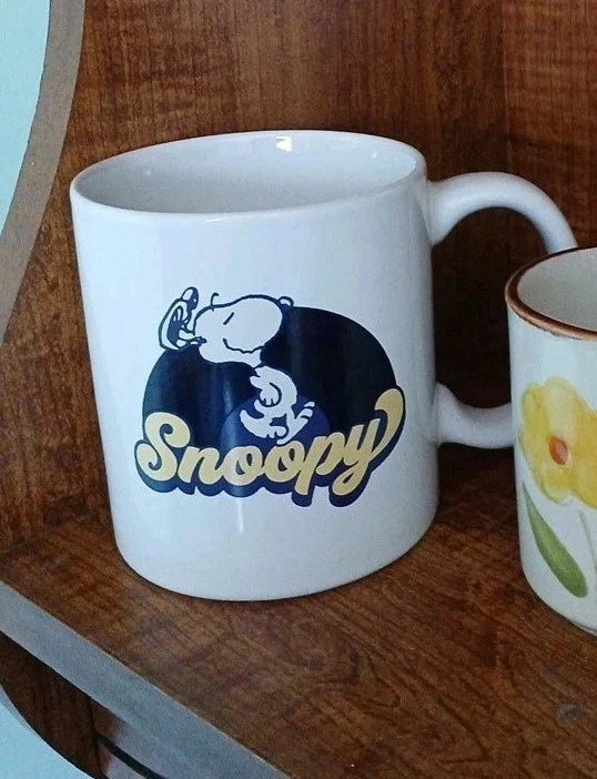 White mug with Snoopy logo on a wooden surface