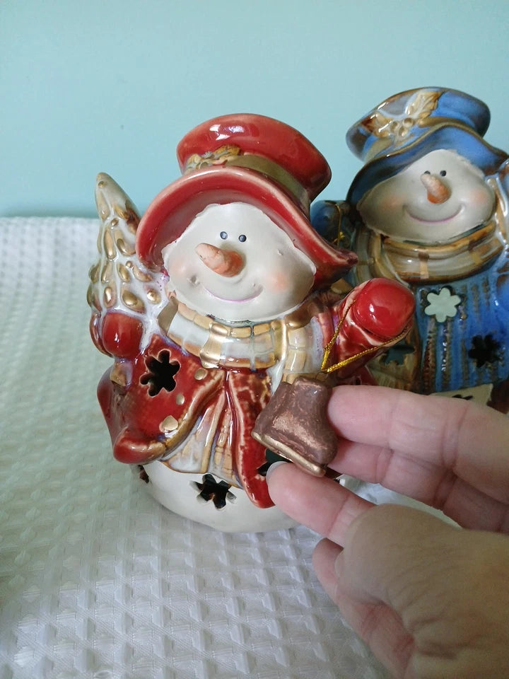 Decorative snowman figurine with a hand holding a small object against a light blue background.
