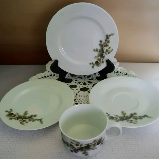 Ceramic tea set with a cup, saucer, and plate featuring green floral patterns on a white surface.