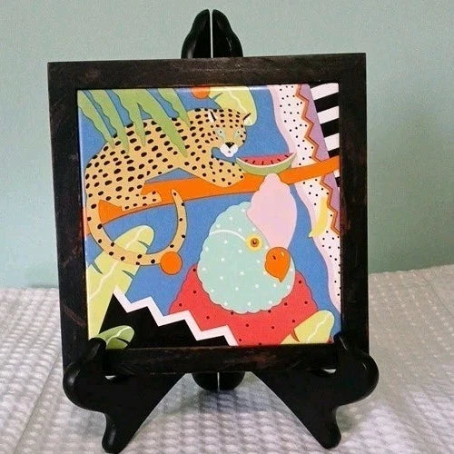 Colorful artwork of a leopard and parrot on a black easel against a light blue wall.